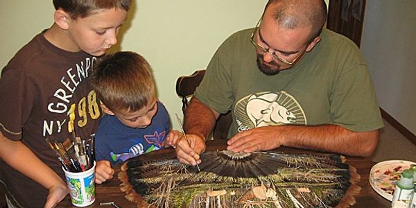 Erich Carlson, artist, demonstrating painting technique on turkey feathers with his boys watching.