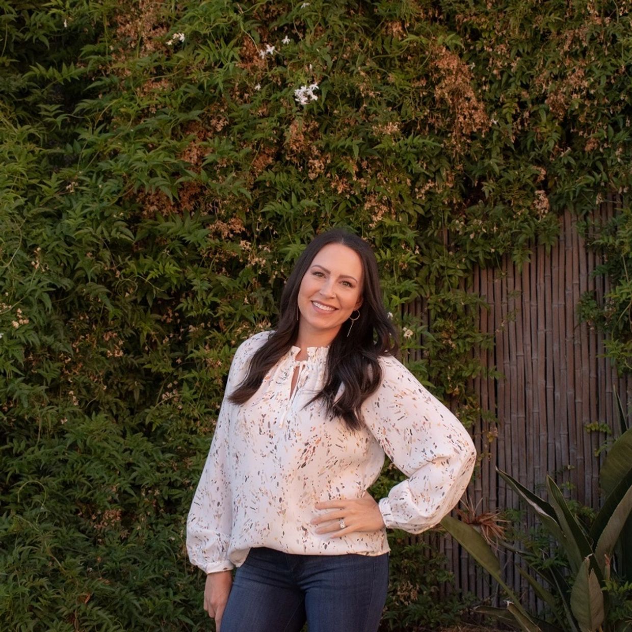 Online therapist smiling and posing while standing in front of a fence with greenery.