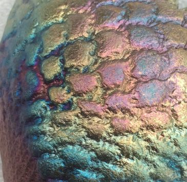 Close up of art piece textured surface showing iridescent rainbow colours of a Raku glaze ceramic