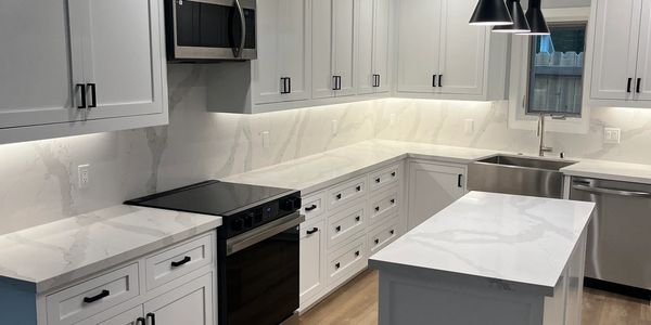 Modern white kitchen with marble countertops and black hardware. Under cabinet led lights and pendent lights over island.