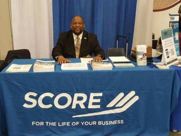 Man sitting at SCORE booth with business brochures.