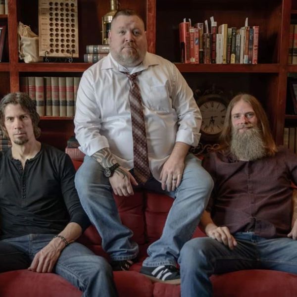 Three men sitting on a couch in a library room.