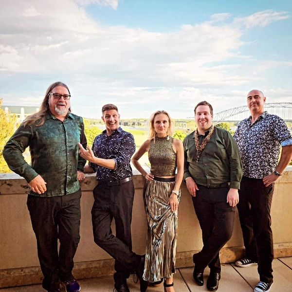 Five people posing outdoors on a balcony under a partly cloudy sky.
