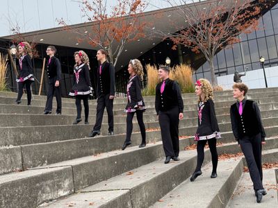 Group of young Irish dancers in traditional costumes posing on outdoor steps.