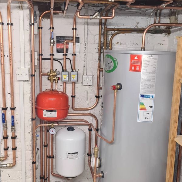 Neatly organized plumbing system with copper pipes and tanks in a utility room.