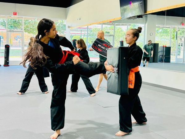 Two martial artists practicing kicks and blocks in a dojo.