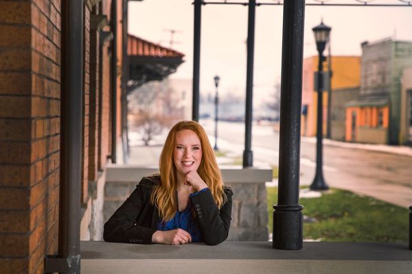 Rosemary Oskvarek sitting near a lamp post and brick building smiling at the camera.