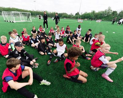 Children sitting on a soccer field during practice or training session.