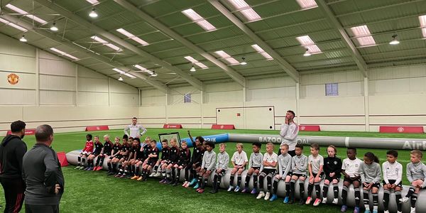 Young soccer players and coaches seated indoors on artificial turf during a training session.
