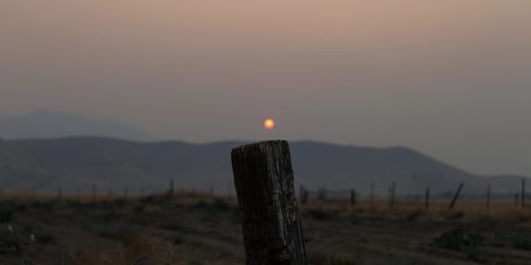 Sun setting over a rural landscape with a wooden post in the foreground.