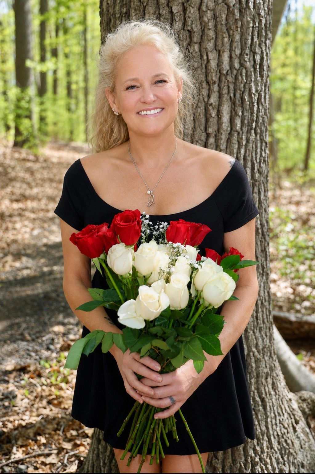 Smiling woman in black dress holding red and white roses in a forest setting.