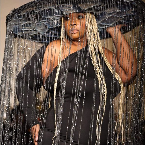 Person wearing a large black hat with hanging silver chains and a black outfit.