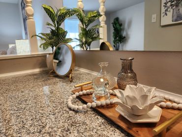 Vanity vignette featuring white ceramic rose, glass bottles, beads and round gold mirror