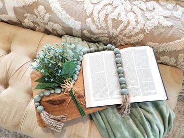 Wooden beads draped over tied bunch of blue flowers and open book at end of bed