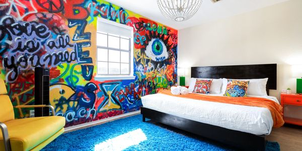 Colorful, urban bedroom with mural of eyeball and round chandelier. 