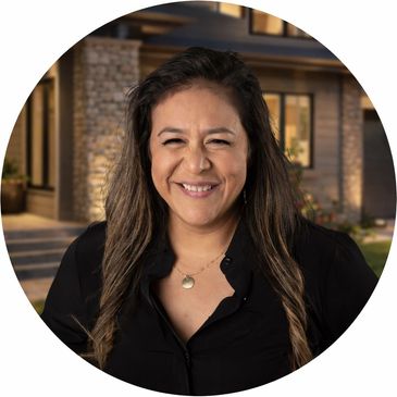 Smiling woman with long hair in front of a house exterior at dusk.