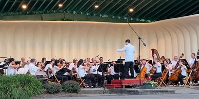 An orchestra performing with a conductor on stage in a modern concert hall.