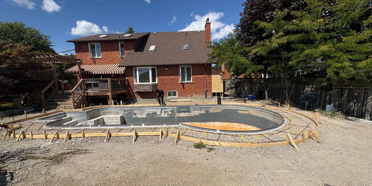 Construction of an in-ground swimming pool in a backyard with a brick house in the background.
