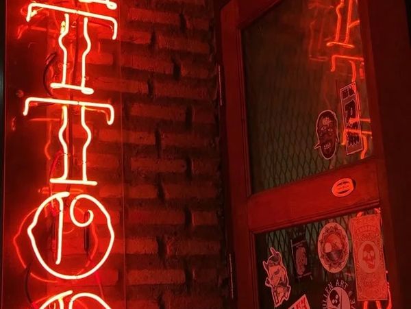 Colored sign showing "Tattoo" in neon red hanging with a brick backdrop.