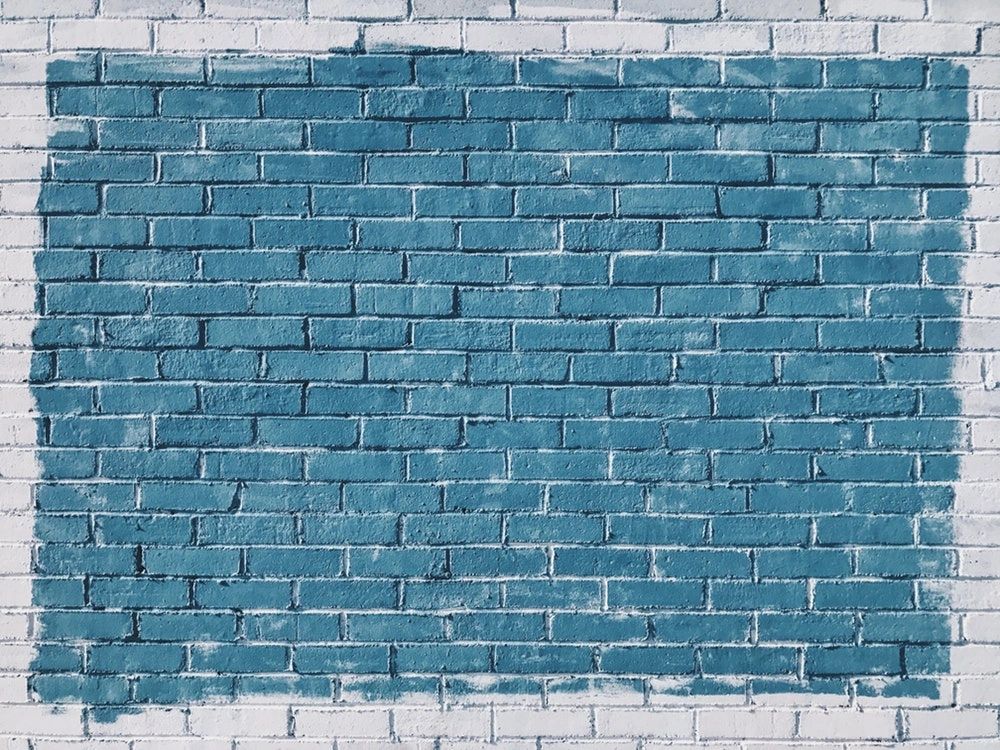 A photo of a white brick wall. The photo frames a portion of the brick wall that is painted blue.