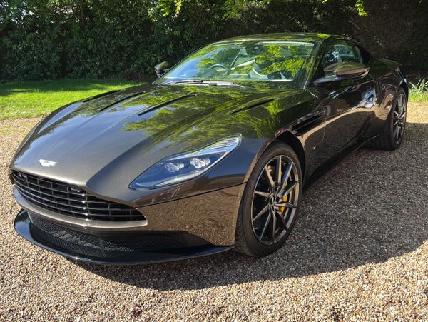 Sleek black Aston Martin sports car parked on gravel under green trees.