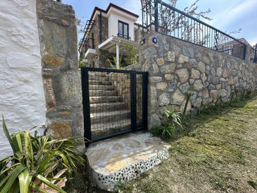 Stone wall and steps with a black metal gate leading to a house.