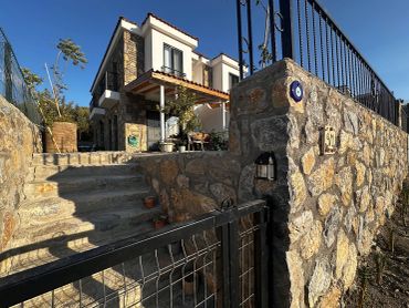 Stone house with a garden and metal gate under clear blue sky.