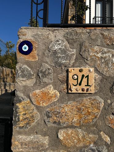 Stone wall with a house number plaque and a blue evil eye charm.