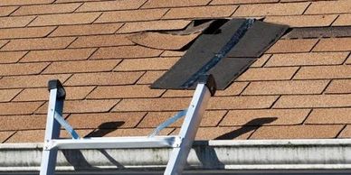 A damaged roof with a hole and a ladder leaning against the gutter.