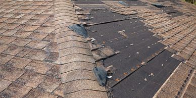 Damaged roof with missing shingles exposing black underlayment.