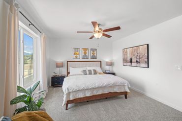 Modern bedroom with a large bed, ceiling fan, and natural light.