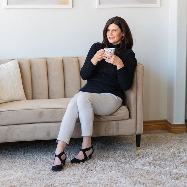 Woman in black sweater enjoying a cup of coffee on a beige couch.