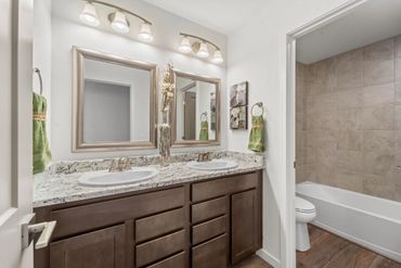 Modern bathroom with dual sinks, granite countertop, and a bathtub with tiled walls.