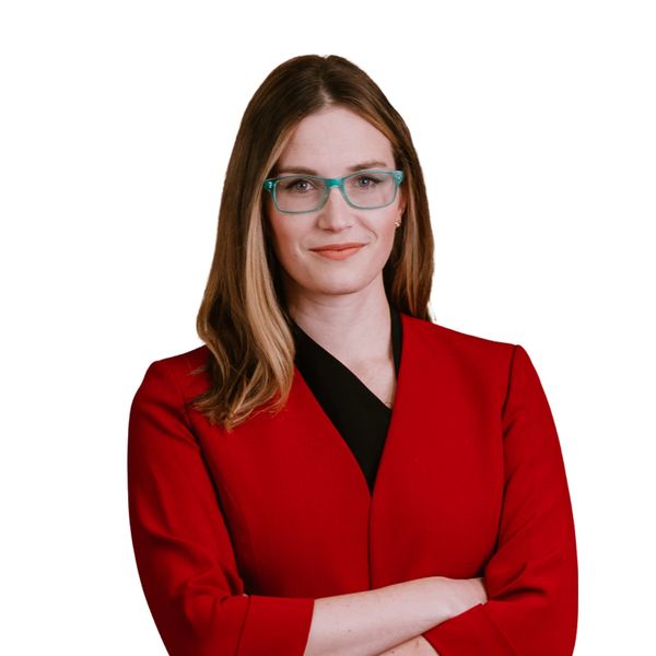 Confident woman in red blazer with teal glasses, arms crossed, smiling.
