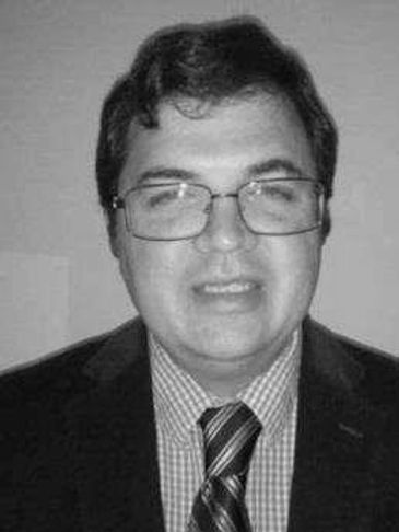 Man wearing glasses, suit, and striped tie smiling.