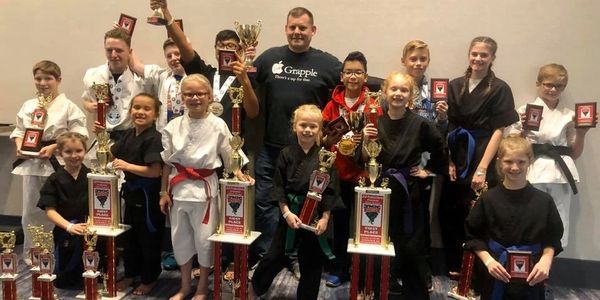 Group of kids in karate uniforms smiling with trophies.