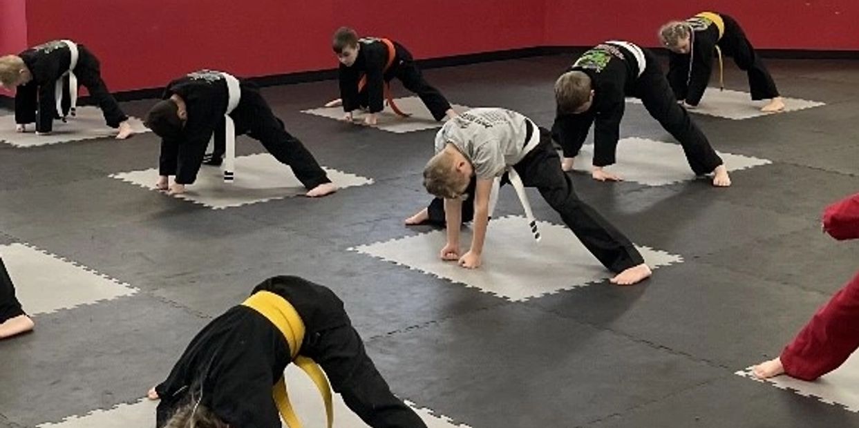 Group of kids in karate uniforms and belts stretching.