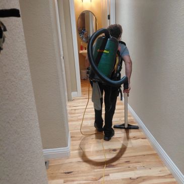 Person vacuuming wooden floor in hallway.