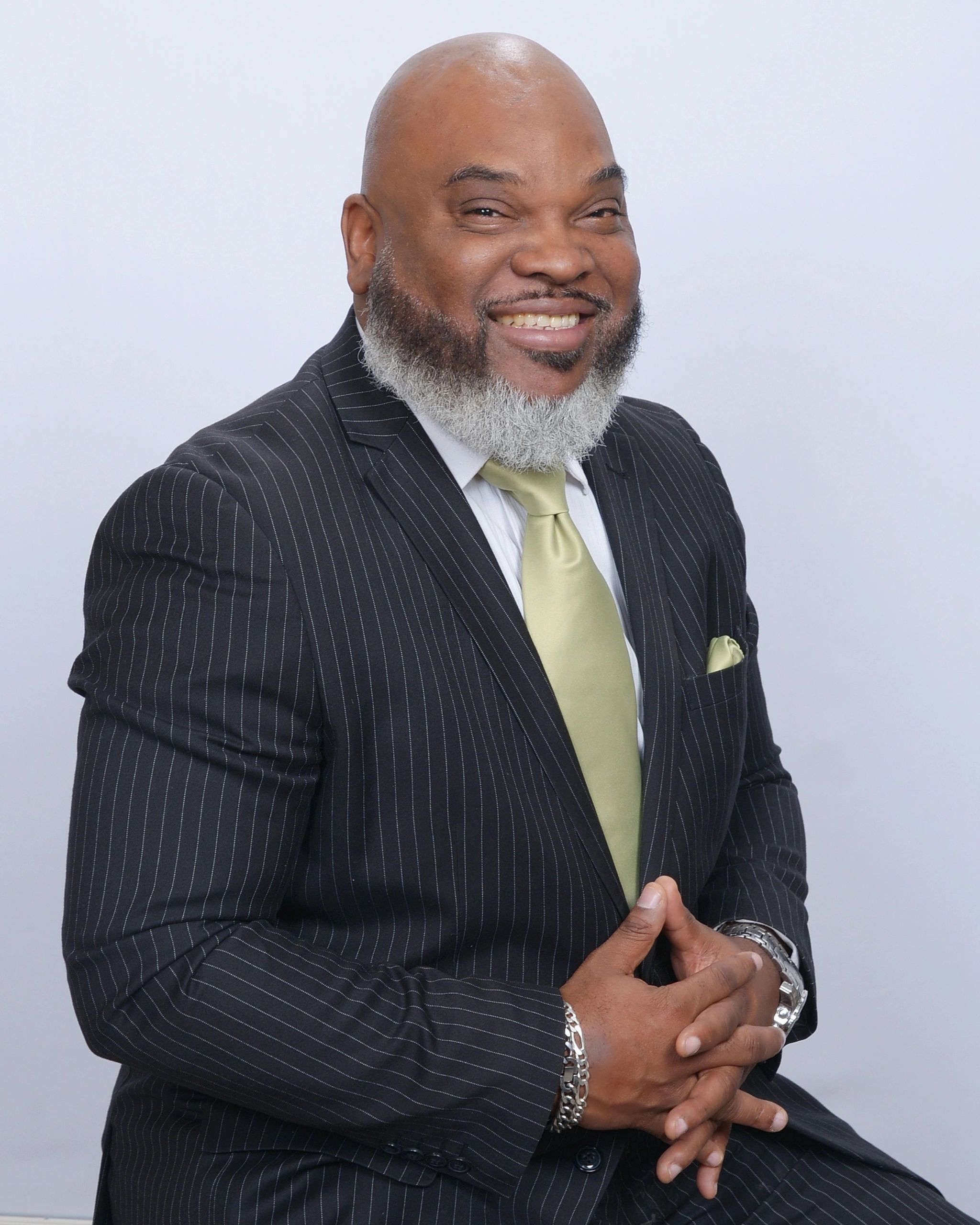 Smiling man in a pinstripe suit with a green tie and white beard.