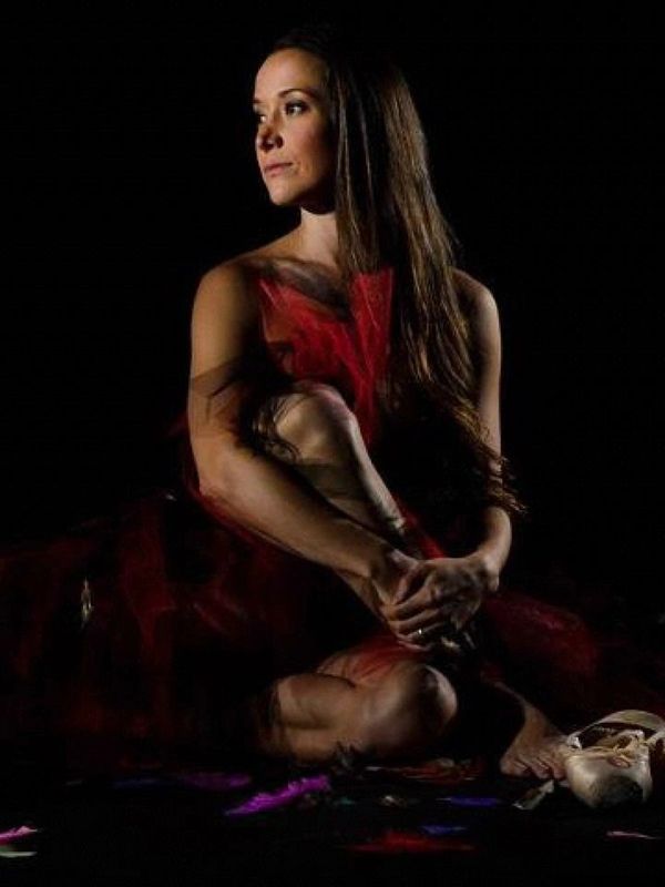 Courta seated on the floor with a red and black tutu and point shoes around her. 
Photograph by Stef