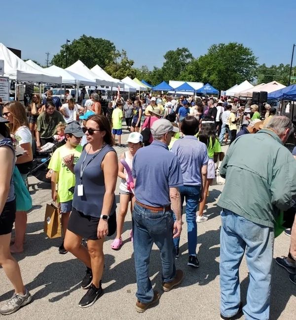 Crowded outdoor event with people walking and socializing under tents.