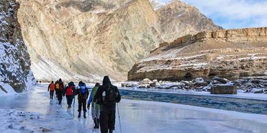 Group trekking on icy terrain beside frozen water and rocky mountains.