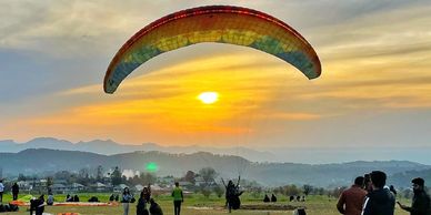 Paragliding at sunset with a crowd watching.
