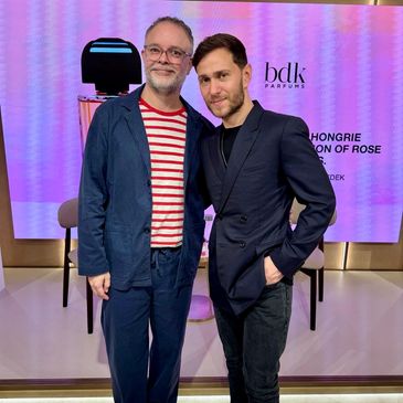 Two men posing in front of a purple-lit backdrop with BDK Parfums branding.