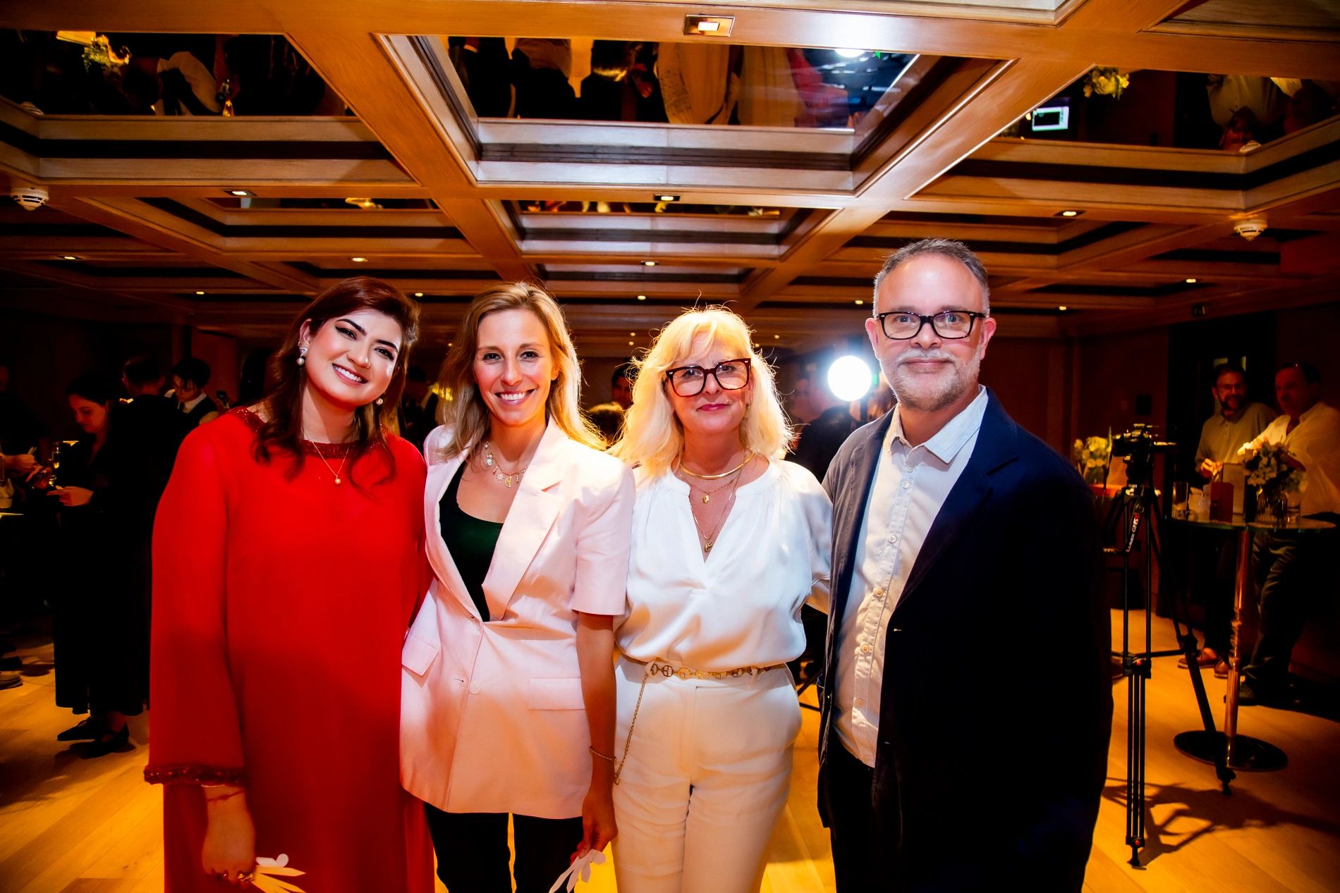 Four well-dressed people smiling at a social event in a warmly lit room.