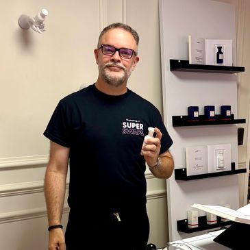 Man holding a white bottle in a fragrance store wearing a Super Swaps shirt.