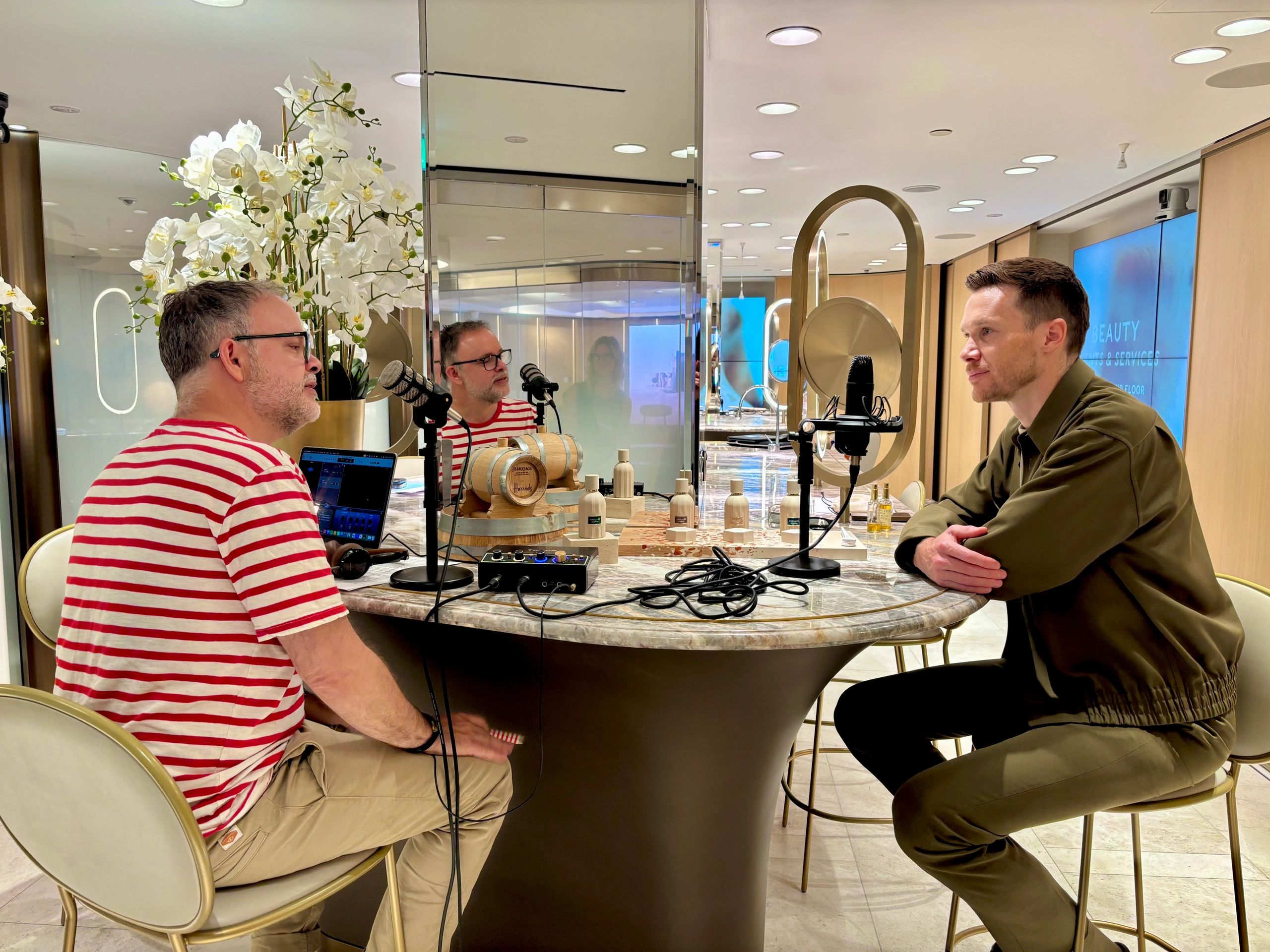 Two men recording a podcast at a stylish table with microphones and a laptop.