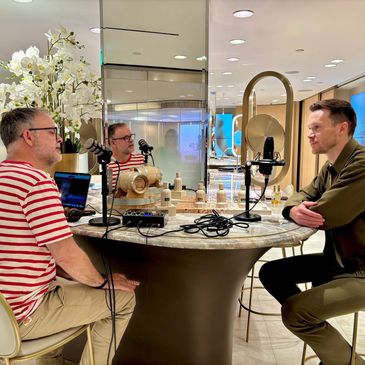 Two men recording a podcast at a stylish table with microphones and a laptop.