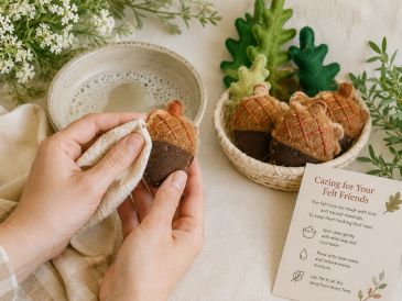 Hands holding a felt acorn next to a basket with more felt acorns.