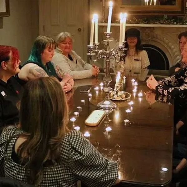 A group of people sitting around a table with candles, possibly in a séance or ritual.